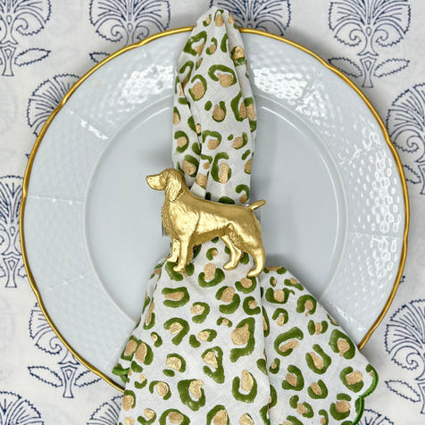 A napkin ring featuring a gold Springer Spaniel design, placed on a napkin with a leopard print pattern, presented on a white plate with a blue and white patterned tablecloth in the background.