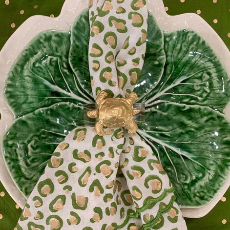 A decorative acrylic and gold leaf napkin ring designed to resemble a turtle, with a green and white patterned napkin.